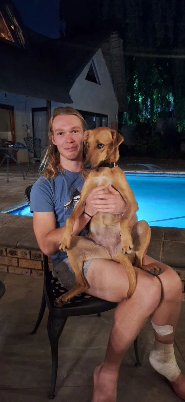 Tiaan sitting beside the pool at night with a dog on his lap.